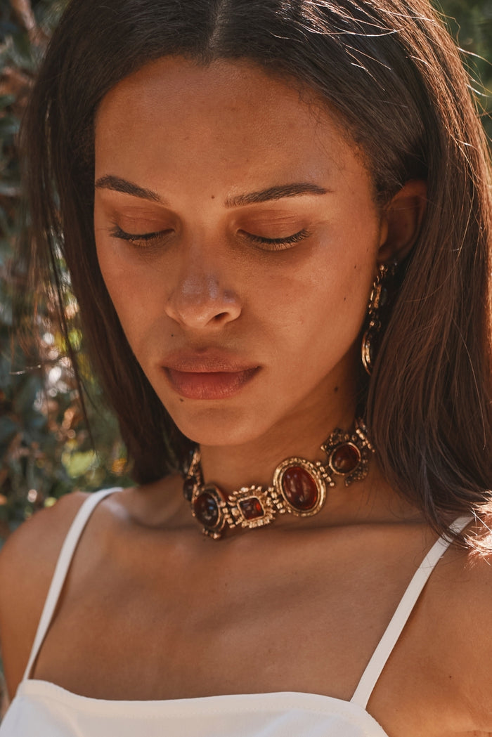 Close-up of a gold amber stone choker worn with a white satin cami outdoors.