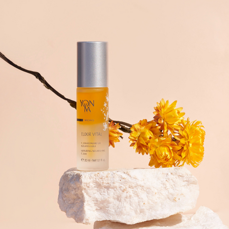 Elixir Vital Repairing Face Oil | Yon-Ka Paris bottle displayed on natural stone with yellow flowers, highlighting skincare and wellness product elegance.