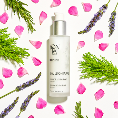 Emulsion Pure Purifying Tonic | Yon-Ka Paris bottle surrounded by fresh green leaves, lavender sprigs, and scattered pink rose petals on a white background, showcasing skincare and wellness.