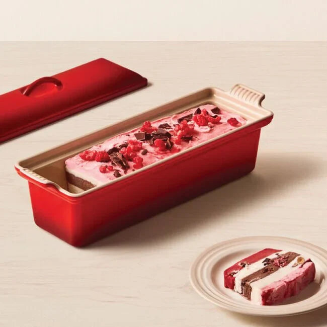 Red terrine mold with pastry and berries, on a beige surface.