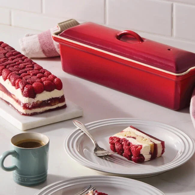 Red ceramic baking dish with raspberry dessert on a white surface