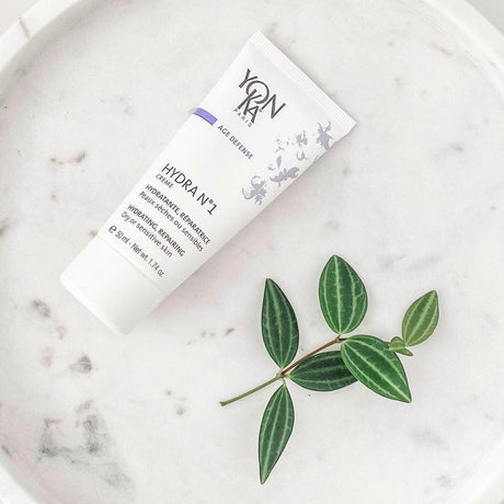 Hydra No. 1 Crème Hyluaronic Acid Moisturizer | Yon-Ka Paris tube placed on a marble surface next to a small green leafy branch, highlighting skincare and wellness.