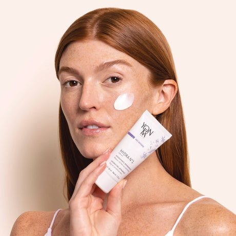A woman with red hair applying Hydra No. 1 Crème Hyluaronic Acid Moisturizer | Yon-Ka Paris to her cheek, showcasing smooth skin and skincare routine.