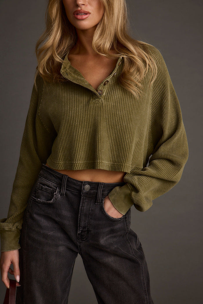 Cropped olive waffle knit henley with button placket, styled on-model over black jeans.