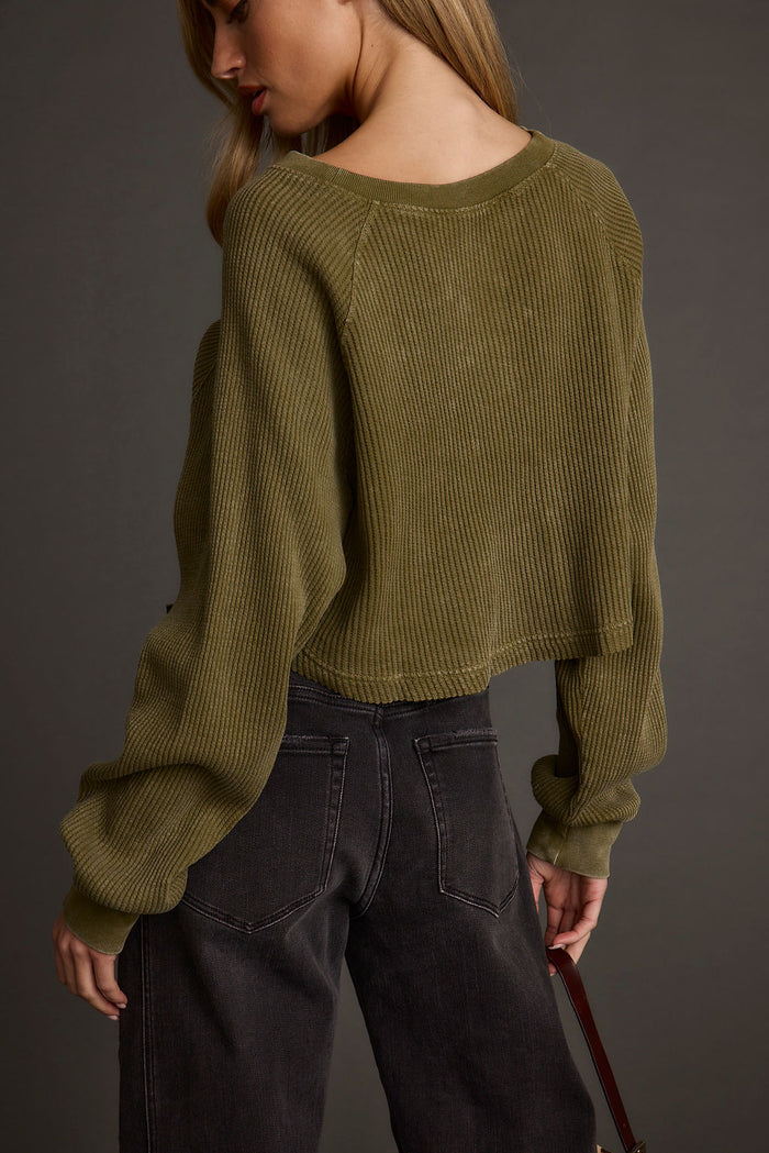 Back view of an olive waffle knit henley worn cropped over faded black wide-leg jeans.
