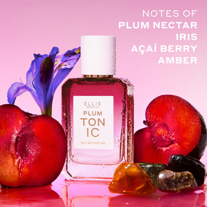 PLUM TONIC Eau de Parfum 50ml next to sliced plums, amber stones and a purple iris covered in water droplets on a pink background with white text that reads "Notes of plum nectar, iris, açaí berry, amber"