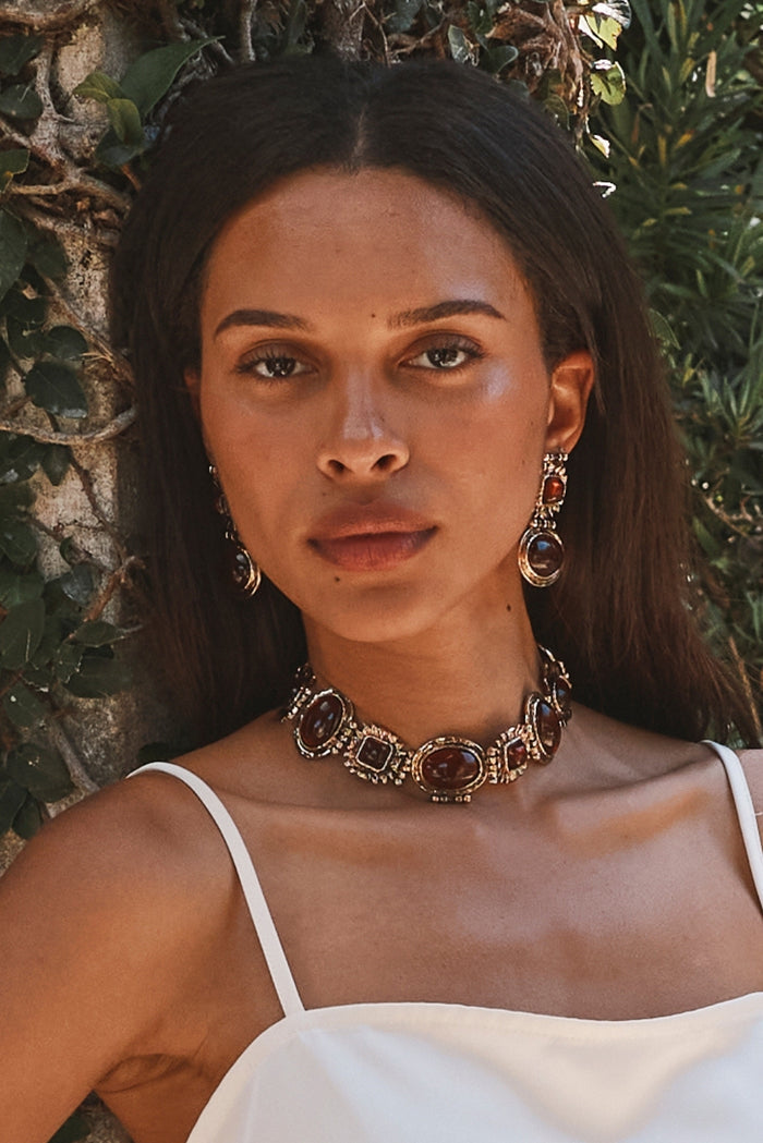 Amber stone drop earrings and matching choker styled with a white satin cami outdoors.