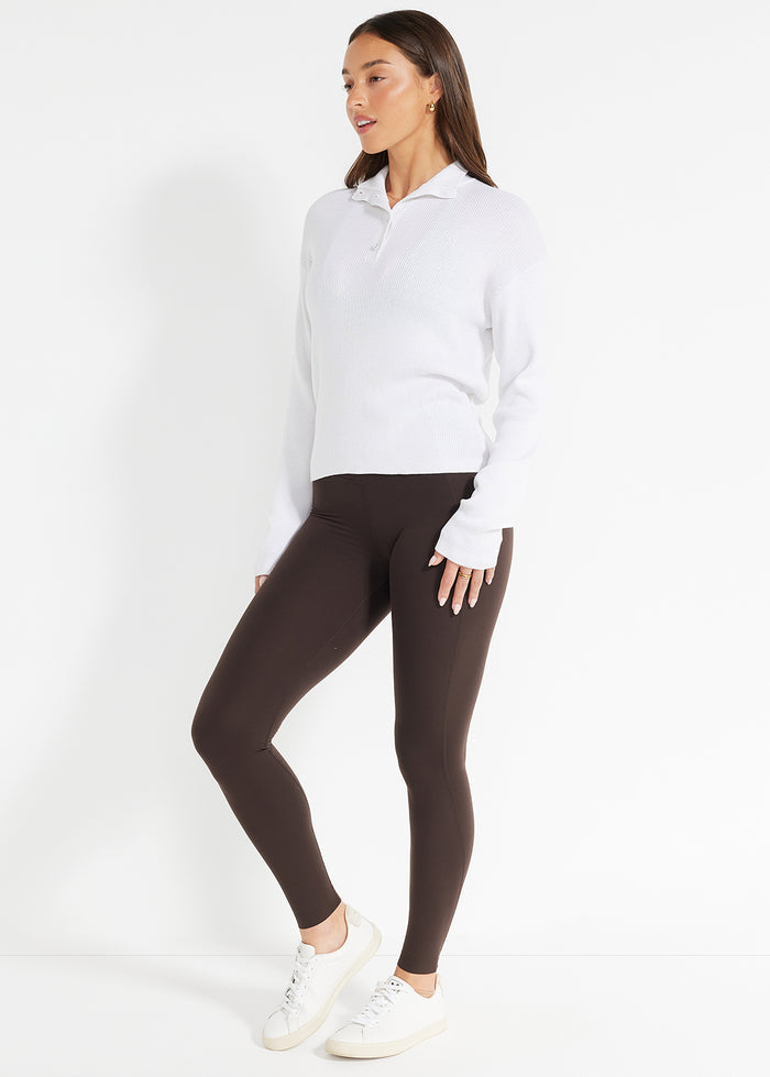 Model wearing white ribbed henley jumper paired with brown leggings and white sneakers